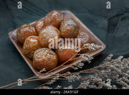 Tre prugne cinesi aromatizzate conservate (frutta conservata) su piatto di legno. Il sapore è acido, salato e dolce. Spazio per il testo, Focu selettivo Foto Stock