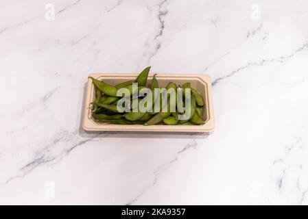 Piccolo vassoio di consegna in cartone pieno di baccelli di edamame su una superficie di marmo bianco Foto Stock