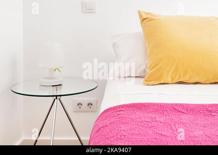 Camera da letto con letto matrimoniale con cuscini in velluto giallo, comodini in vetro e pareti dipinte di bianco Foto Stock