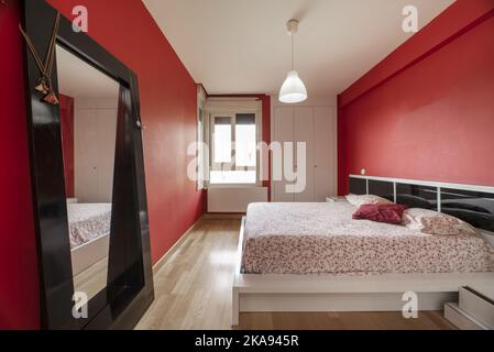 Camera da letto con pareti dipinte di rosso luminoso, accenti di specchio nero e testata bianca e armadio incorporato Foto Stock