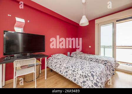 Camera da letto con pareti dipinte di rosso luminoso, letti singoli e un tavolo da studio con schermo TV Foto Stock