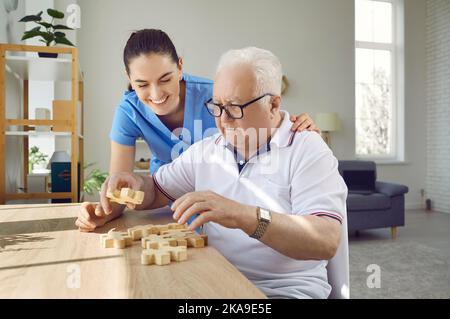 Infermiera in casa di riposo aiutare l'uomo anziano con Alzheimer per costruire puzzle jigsaw Foto Stock