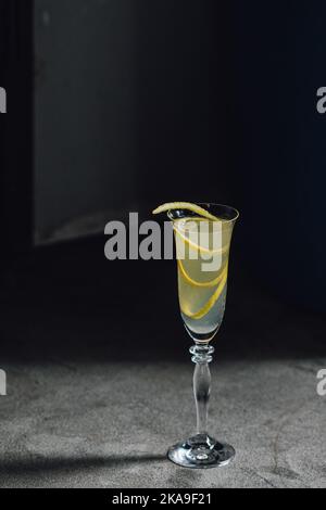 cocktail francese di champagne 75 con tocco limone guarnire in flauto vetro contro cemento rustico metallo Foto Stock