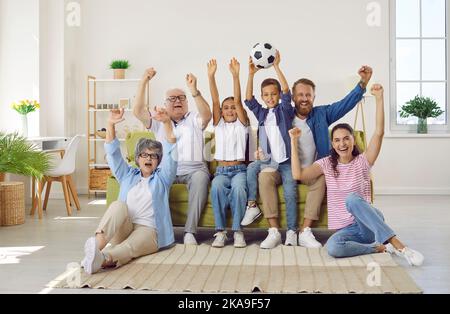 Una grande famiglia entusiasta che mostra un gesto di vittoria mentre guarda il campionato di calcio in TV. Foto Stock