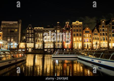 La strada principale di Damrak Amsterdam Paesi bassi con case da ballo e riflessione in acqua di notte con le barche Foto Stock