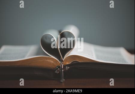 Apri il libro spirituale della sacra bibbia con la pagina a forma di cuore piegata al centro e la collana a croce. Foto Stock
