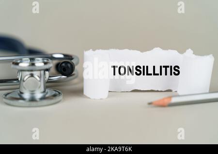 Concetto medico. Su sfondo grigio, uno stetoscopio, una matita e una lastra di carta con l'iscrizione - Tonsillitis Foto Stock