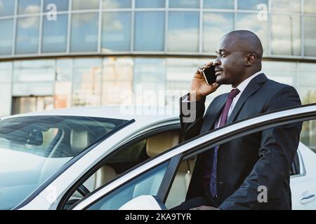 Il ritratto di un bell'uomo d'affari afroamericano di successo in una tuta si trova vicino alla sua auto Foto Stock