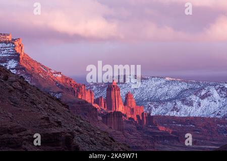 Fisher Towers sul fiume Colorado ghiacciato al tramonto in inverno con le montagne la SAL dietro. Vicino a Moab, Utah. Foto Stock