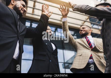 Team internazionale di imprese di persone di successo che celebrano la vittoria. Gli uomini in tute in una riunione aziendale gioiscono per i risultati della loro azienda Foto Stock