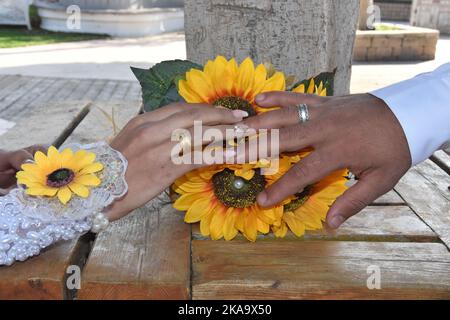 mani di sposi novelli con anelli di nozze d'oro, fiori gialli Foto Stock