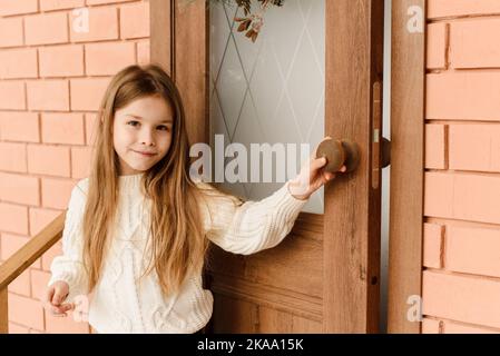 La bambina carina apre la porta con una corona di Natale Foto Stock