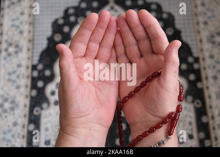 Un uomo anziano che prega sul tappeto di preghiera semplicemente mostrando le mani con perline di preghiera. Mani ravvicinate con perle che pregano per Dio. İslamic concetto backgroun Foto Stock