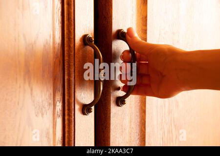 La mano di una donna strappa un vecchio armadio di legno, apre la porta di un armadio di biancheria, una maniglia sulle porte di mobili Foto Stock