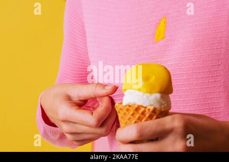 Mano femmina che mostra una macchia sporca cremoso gelato di banana sulla blusa. Isolato. Su sfondo giallo Foto Stock
