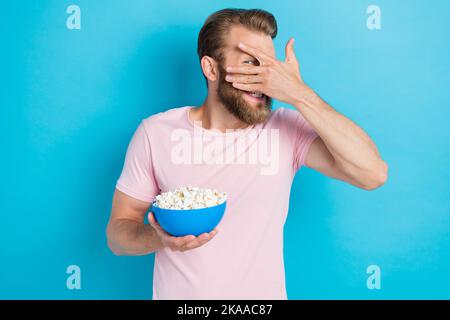 Ritratto fotografico di bel giovane ragazzo tenere popcorn ciotola guardare film horror vestito elegante look rosa isolato su sfondo color acquamarina Foto Stock