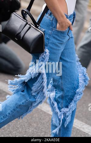 Milano, Italia - 21 settembre 2022: Donna che indossa pantaloni con frange in denim blu e borsa domenicale in pelle nera dell'Attico, outfit Street style. Foto Stock