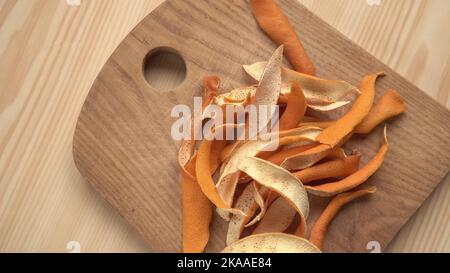 Bucce di frutta secca d'arancia su un tagliere di legno sul tavolo in primo piano - le spezie per bevande calde e cibo. Un modo per aggiungere sapore al pasto. Foto Stock