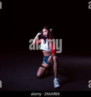 Giovane donna che tiene la pistola d'acqua vestita in costume di Harlequin su una strada di Asphalt Foto Stock