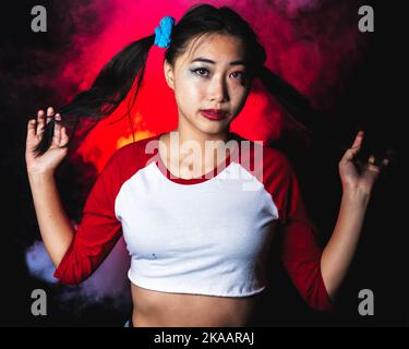 Giovane donna in costume di Harlequin in piedi di fronte a nebbia luminosa | Ritratto della macchina della nebbia Foto Stock