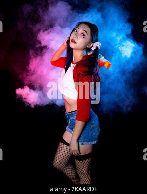 Giovane donna in costume di Harlequin in piedi di fronte a nebbia luminosa | Ritratto della macchina della nebbia Foto Stock