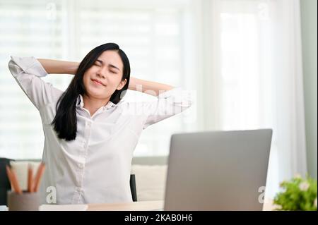 Attraente giovane donna d'affari asiatica o donne manager mani dietro la testa, gli occhi chiusi, rilassarsi alla sua scrivania in ufficio. Foto Stock