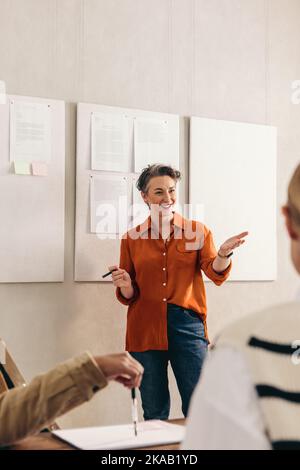 Allegra donna d'affari che presenta la sua idea al suo team durante una riunione. Buon team leader che ha avuto una discussione con i suoi colleghi. Gruppo di creativi bu Foto Stock