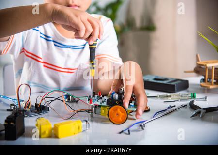 Ragazzo asiatico che monta il progetto di lavoro dell'auto robot Arduino a casa Foto Stock