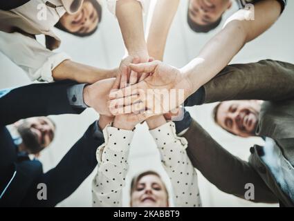 Mirare al successo . Inquadratura ad angolo basso di un gruppo di uomini d'affari allegri che formano una huddle con le mani e che guardano verso il basso all'interno dell'ufficio. Foto Stock