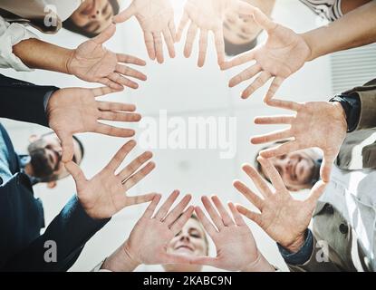 Questo è l'aspetto delle mani di lavoro. Inquadratura ad angolo basso di un gruppo di uomini d'affari allegri che formano una huddle con le mani e che guardano verso il basso all'interno Foto Stock