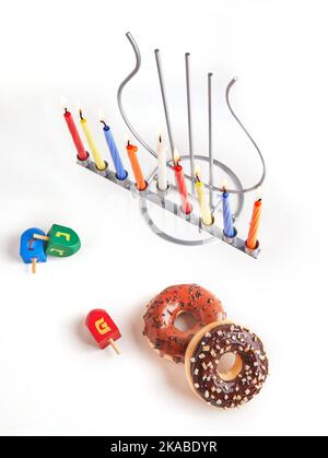 Vacanza ebraica sfondo Hanukkah. Il piatto tradizionale è costituito da ciambelle dolci. Hanukkah tavolo impostazione candelabro con candele e spinning cime su bianco Foto Stock