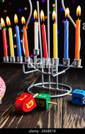 Vacanza ebraica sfondo Hanukkah. Il piatto tradizionale è costituito da ciambelle dolci. Hanukkah tavolo impostazione candelabro con candele e spinning cime sul nero Foto Stock