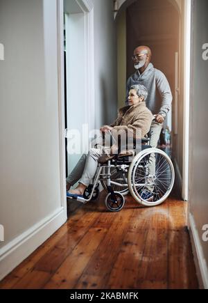 HES è ancora un Signore dopo tutti questi anni. Scatto a tutta lunghezza di un uomo anziano che spinge la moglie legata alla sedia a rotelle attraverso la casa. Foto Stock