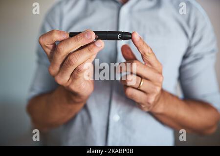 Il mio piccolo salvavita. Un uomo irriconoscibile che tiene una penna per iniezione di insulina con le mani a casa durante il giorno. Foto Stock