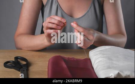 Le mani femmina inseriscono il filo attraverso il piccolo foro dell'ago per cucire. Foto Stock