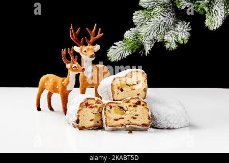 Fette di stollen dolce con noci e frutta secca su tavola con cervi giocattolo e ramo di abete rosso innevato Foto Stock