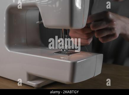 Mani inserire il filo attraverso il foro dell'ago nella macchina da cucire, dettagli. Foto Stock