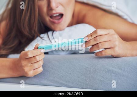 Giovane donna brunetta con test di gravidanza a letto Foto Stock