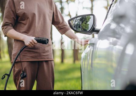 Immagine a colori di una mano di un uomo la preparazione per caricare un auto elettrica. Foto Stock