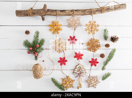 Garland di Capodanno di fiocchi di neve di legno su un ramo di legno spesso. Rami verdi di abete rosso, coni. Fondo di legno bianco fatto di tavole Foto Stock