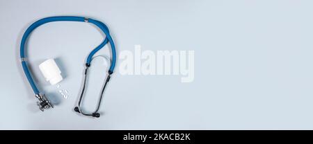 Stetoscopio e vasetto di pillole bianche su sfondo blu. Concetto medico e cardio di salute del cuore. Banner con spazio di copia per il testo. Foto Stock