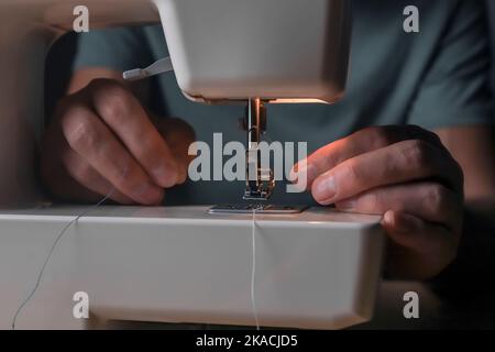 Mani che inseriscono il filo attraverso il foro dell'ago nella macchina da cucire, primo piano. Foto Stock