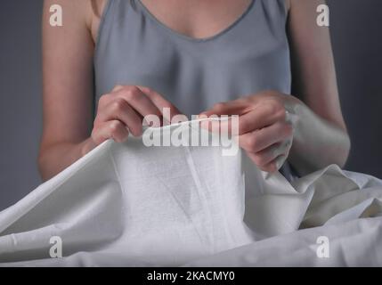 Le mani inseriscono il filo attraverso il foro dell'ago per cucire alla sua scrivania di legno. Foto Stock