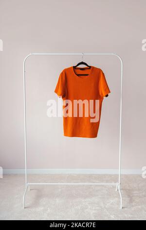 T-Shirt bianca Mock-up appeso al gancio per rack bianco, vista frontale Foto Stock