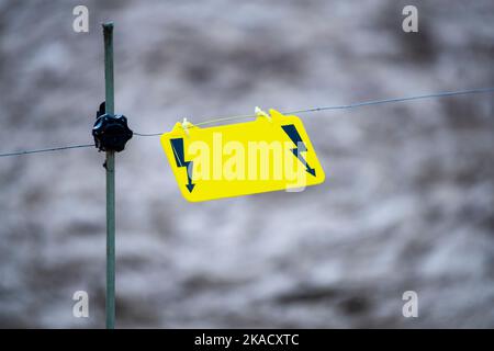 Segnale di avvertenza recinzione elettrica. Un segnale di avvertimento giallo è appeso su un filo e avverte di pericolo. Foto Stock