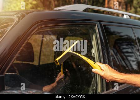 Mano con scraper auto in gomma pulire il finestrino automatico all'esterno. Foto Stock