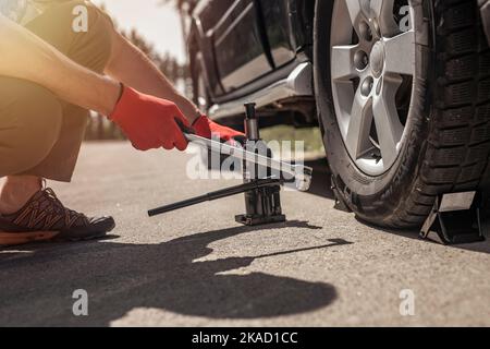 Il martinetto idraulico per auto viene messo sotto auto con le mani in guanti, primo piano. Foto Stock