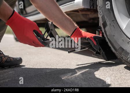 Mettere a mano dei cunei sotto lo pneumatico dell'auto su strada, vista dal basso. Foto Stock