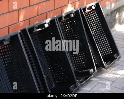 Quattro casse vuote di plastica nera per frutta e verdura appoggiate contro la parete di mattoni all'aperto Foto Stock