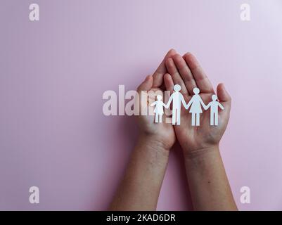 mani che tengono la famiglia cutout di carta, assicurazione contro le malattie di vita, concetto di distensione sociale, covid19, sullo sfondo di colore rosa, protezione della famiglia Foto Stock